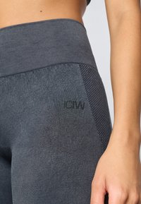 Φαρδιά ψηλόμεση, σκούρη γκρι κολάν με ραβδωτή ζώνη και μπροστινές υφές. Μικρό, ανάγλυφο λογότυπο κοντά στους γοφούς. Λείο ύφασμα.