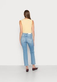 Top sem mangas amarelo-claro, jeans de cintura alta azul-claro com corte reto e sapatos planos bordeaux. Tecido suave e design simples.