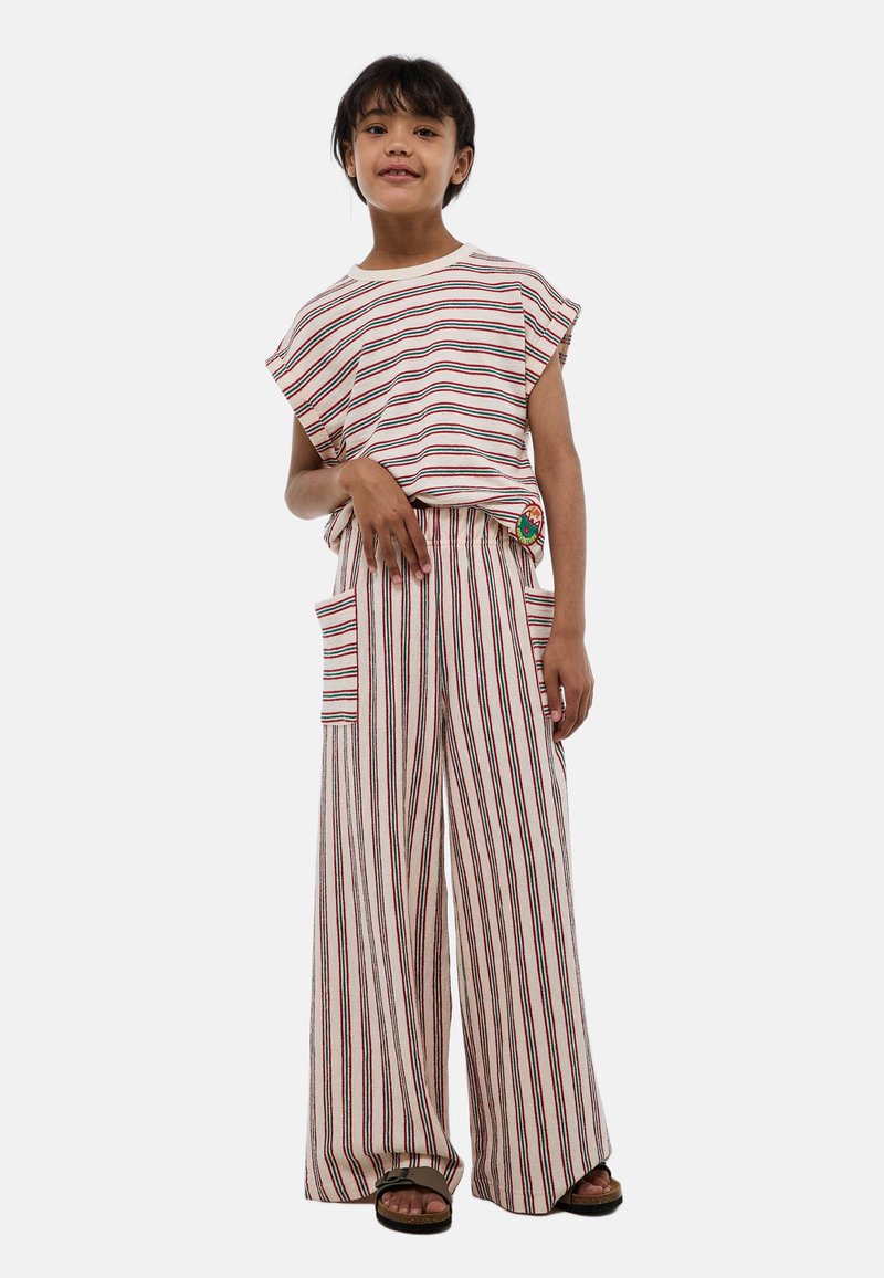 Fille debout portant un haut sans manches blanc à rayures et un pantalon large avec de grandes poches et des sandales.