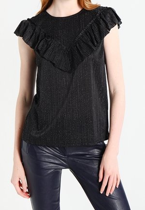 Kvinde iført sort kortærmet top med flæset V-detalje og teksturerede lodrette striber, kombineret med mørke læderbukser.