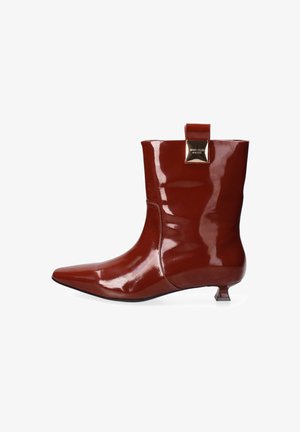 Bottine en cuir verni rouge avec un bout pointu, un petit talon carré et un accent décoratif en métal doré à l'arrière. Fini lisse et brillant.