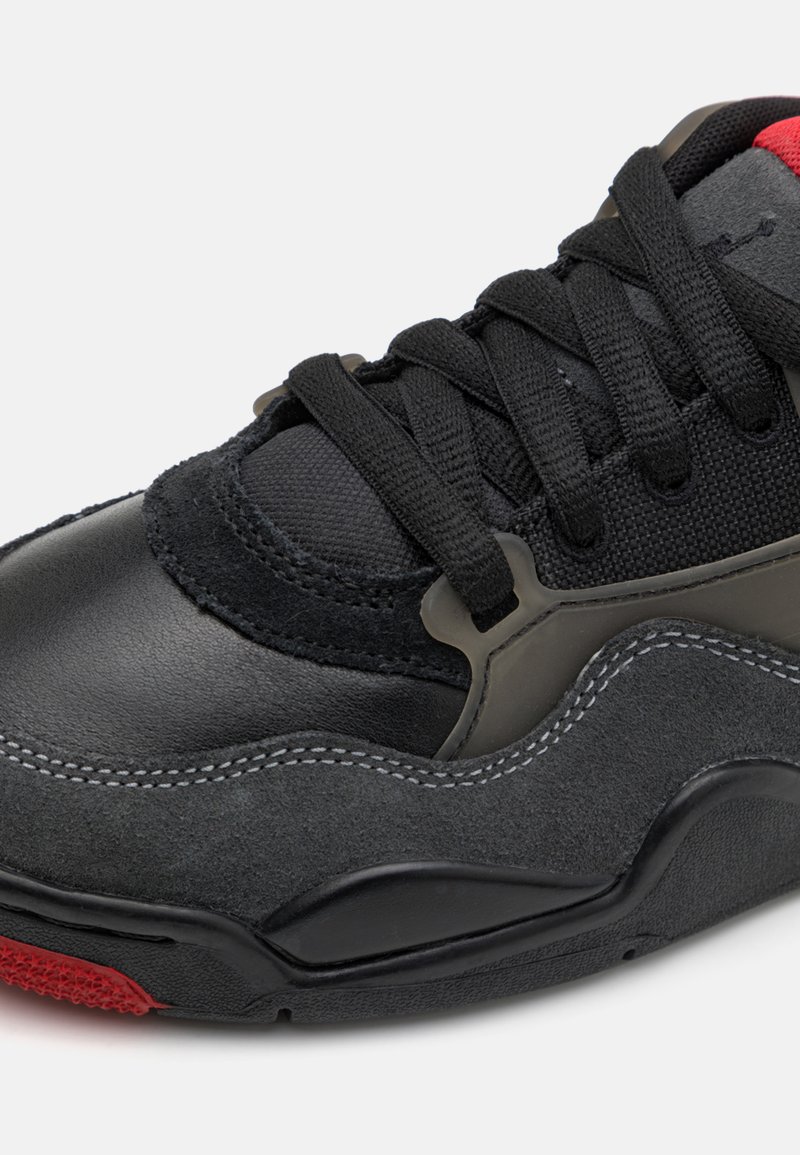 Zapatilla negra y gris que presenta una combinación de materiales de cuero y ante, con cordones negros y un acento rojo en la suela.
