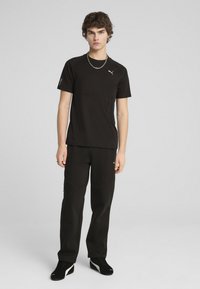 Czarny sportowy T-shirt z krótkim rękawem, z kieszenią na zamek. Zestawiony z czarnymi spodniami dresowymi, oba z gładkiego, oddychającego materiału.