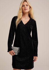 Black velvet dress with long sleeves and a V-neck. The fabric has a subtle sheen, complemented by a small silver and black clutch.