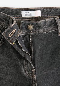 Blugi largi cu talie joasă din denim gri închis, cu cusături contrastante portocalii, fermoar și detaliu cu logo pe talie.