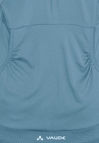 Top atletico azzurro chiaro con dettagli arricciati ai lati, texture liscia e un bordo strutturato all'orlo con il logo "VAUDE".