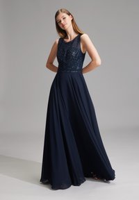 Navy sininen iltapuku, jossa on paljettiliivi, hihaton muotoilu ja virtaava sifonkihame, luoden elegantin siluetin.