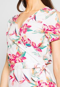 Robe portefeuille blanche à motifs tropicaux colorés. Dotée d'un décolleté en V, de manches courtes et d'une ceinture à nouer à la taille pour un ajustement réglable.