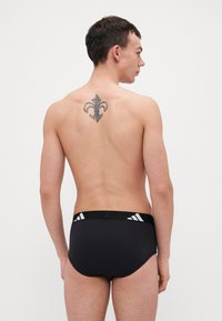 Schwarze Badehosen mit einem figurbetonten Design, ausgestattet mit einem strukturierten Bund und weißen Akzentstreifen an den Seiten. Rückansicht eines männlichen Modells.