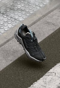 Black hiking shoe with gray accents, textured upper, thin laces, and a rubber sole. Features a loop on the heel for easy wear.