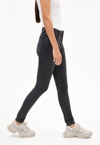 Dunne zwarte jeans van denim, met een hoge taille, vijf zakken en een gladde textuur. Draagt bij lichte sneakers.