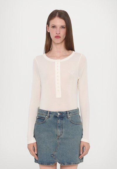 Top crema a maniche lunghe con scollo rotondo e bottoniera, abbinato a una gonna a tubino in denim blu. Dettaglio ricamato discreto sul top.