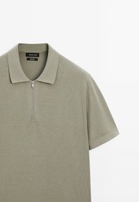Polo tričko s krátkým rukávem ve tlumené zelené barvě, s předním zipem, texturovanou tkaninou a klasickým ribbovaným límcem.