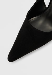 Fekete, süet anyagú, hegyes orrú magassarkú cipő elegáns dizájnnal. Simított belső béléssel és minimalista sziluettel rendelkezik. Látható fémrész vagy díszítés nélkül.