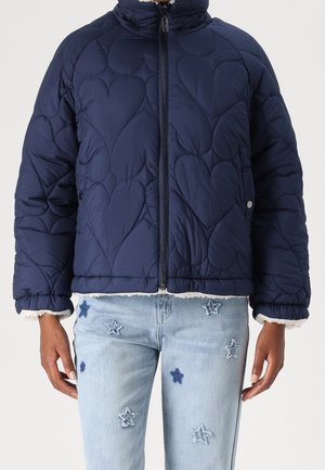 Granatowa pikowana kurtka z przeszyciami w kształcie serc i zamkiem z przodu, noszona z jasnoniebieskimi dżinsami ozdobionymi haftowanymi naszywkami w kształcie gwiazd.