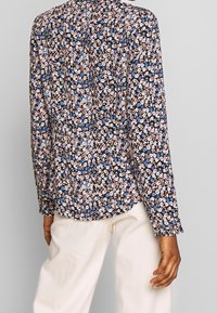 Blusa floreale con uno sfondo nero e fiori rosa e blu, maniche lunghe, colletto e una texture di tessuto morbido.