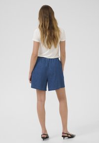 Denim šorti ar brīvu piegriezumu, elastīgu jostu un vienkrāsainu zilu krāsu. Apvienoti ar baltu īsām piedurknēm topu un melnu apavu.