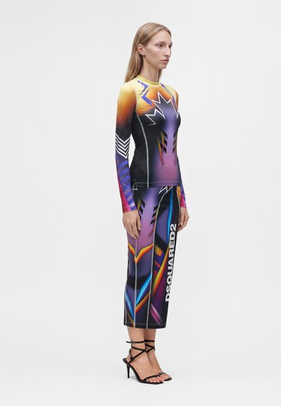 Femme portant un haut à manches longues coloré et à motifs ainsi qu'une jupe assortie aux motifs abstraits et des sandales noires à talons hauts.