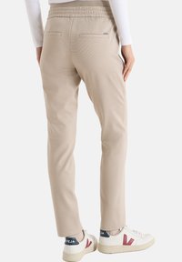 Beige op maat gemaakte joggingbroek met een trekkoord in de taille, achterzakken en een zachte textuur, gecombineerd met witte sneakers met rode accenten.