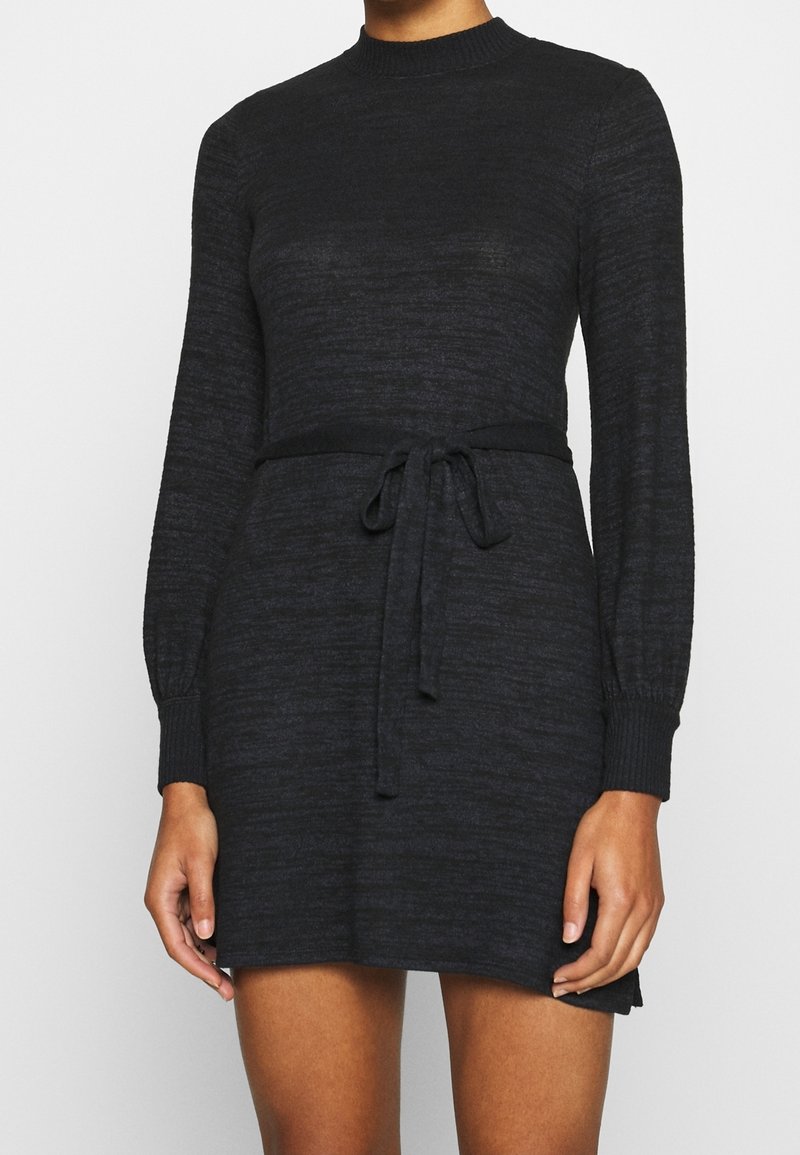 Czarna dzianinowa sukienka z długimi rękawami, okrągłym dekoltem, paskiem w talii i ściągaczami na rękawach. Gładka faktura i luźny krój.