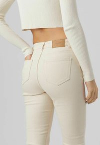 Úzké džíny v off-white látce s hladkou strukturou, které mají dvě zadní kapsy a obdélníkovou hnědou koženou nášivku na pase.