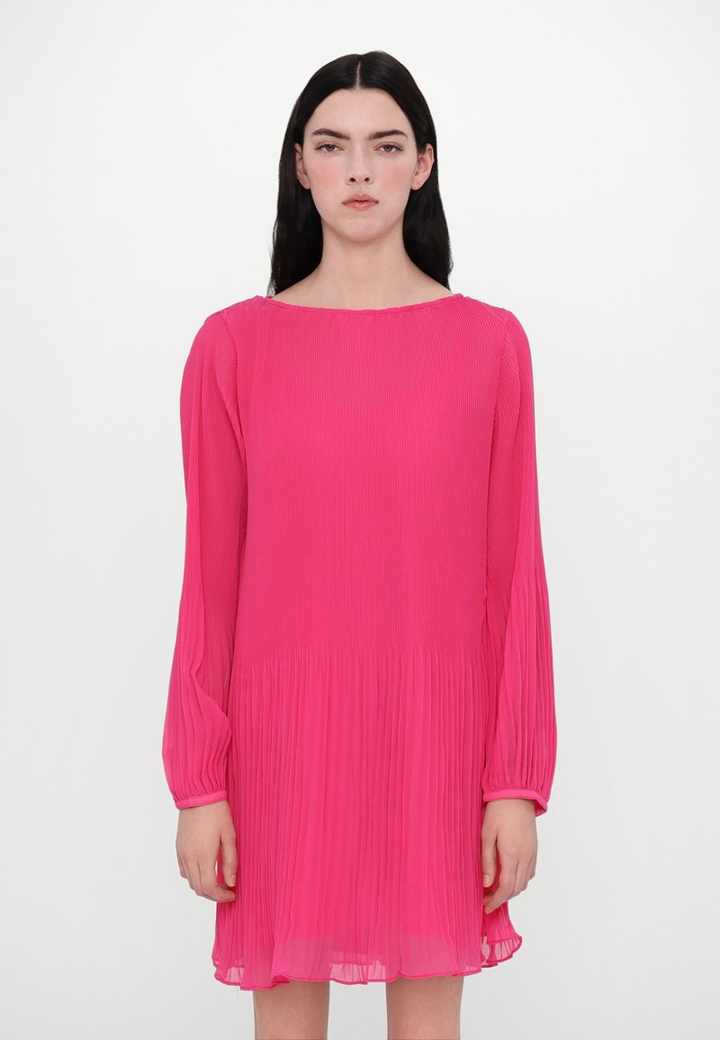 Roze geplooide jurk met lange mouwen, een bootnek en een uitlopende onderkant. Lichtgewicht stof zorgt voor een zachte textuur en beweging.