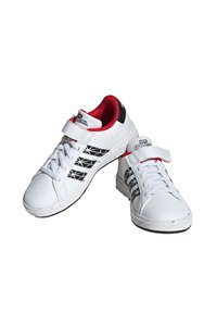Sneakers bianche con strisce nere, rivestimento interno rosso e cinturino in velcro. Presentano una texture liscia e un design con punta arrotondata.