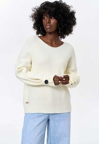Cream ribbed sweater with a wide neckline and oversized sleeves. Features black button accents on the sleeves and a small label at the hem.