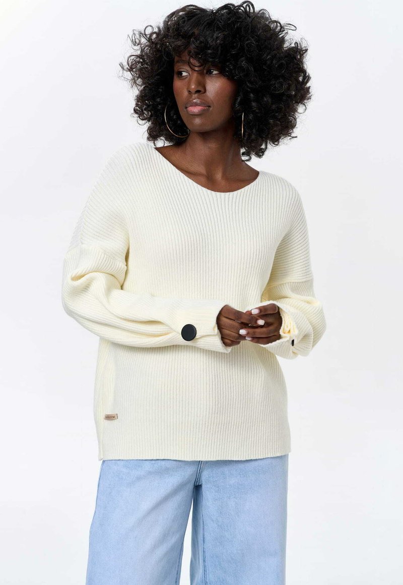 Cream ribbed sweater with a wide neckline and oversized sleeves. Features black button accents on the sleeves and a small label at the hem.