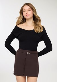 Top nero a maniche lunghe con motivo a coste e design scollato sulle spalle, abbinato a una minigonna marrone con dettaglio alla cintura e texture liscia.