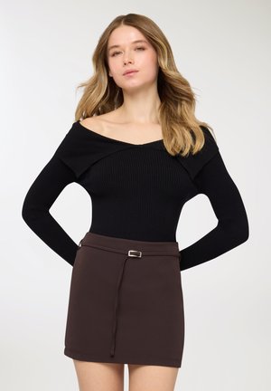 Top nero a maniche lunghe con motivo a coste e design scollato sulle spalle, abbinato a una minigonna marrone con dettaglio alla cintura e texture liscia.