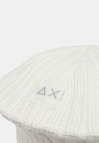 Berretto basco bianco in maglia con texture a coste e una targhetta quadrata in tessuto con un disegno astratto argentato.