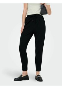 Svarte avsmalnende bukser med elastisk midjebånd og snøring. Glatt stoff med detaljer på sidesømmene. Brukes med svarte loafers og en veske.