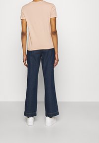 Camiseta de manga corta rosa claro combinada con pantalones vaqueros de pierna ancha azul oscuro y zapatillas blancas, con un diseño simple y colores sólidos.