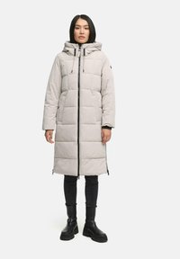 Lange, lichtgrijze pufferjas met een capuchon en een doorgestikt ontwerp. Heeft een rits aan de voorkant en twee zijzakken. Gedeeltelijk gestyled met zwarte skinny jeans en laarzen.