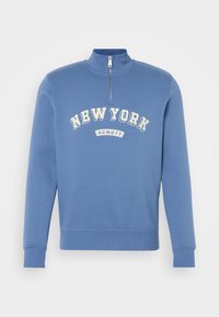 Sweat-shirt bleu à zip quart, avec « NEW YORK » et « SCHOTT » imprimés en lettres blanches sur la poitrine, avec poignets et ourlet côtelés.