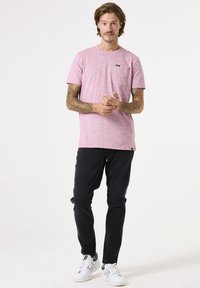 Roze melange t-shirt met een ronde hals en een borstzak, gecombineerd met zwarte slim-fit broek en witte sneakers met groene accenten.