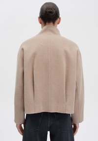 Beige wollen blend jas met een relaxte pasvorm, hoge kraag en verlaagde schouders. Heeft een rechte zoom en subtiele textuur.