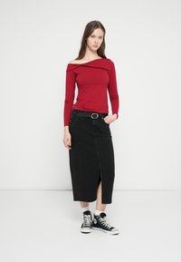 Red long-sleeve top with off-shoulder design, paired with a black denim skirt featuring a front slit, worn with black high-top sneakers.