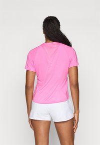 Ružová športová tričko s krátkym rukávom, so štruktúrovaným zadným panelom a zakriveným spodným okrajom, spárované s bielymi šortkami.