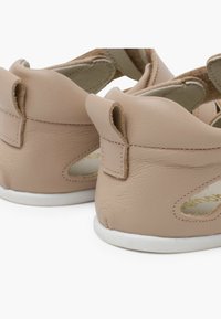Scarpe in pelle rosa chiaro con dettagli intagliati, texture morbida e suole bianche. Presentano piccole linguette sul tallone per facilitarne l'indossamento.