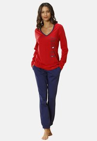 Red long-sleeve top with a V-neck and navy accents, featuring printed text and graphics; paired with navy pants. Soft, casual design.