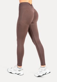 Leggings marron à taille haute avec une finition texturée, coupe ajustée et coutures verticales, associés à des chaussures de sport blanches.