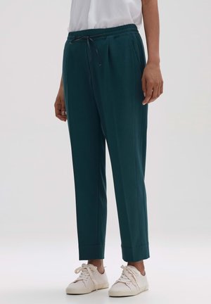 Pantalons de jogging teal avec taille élastique et cordon de serrage, dotés de deux poches latérales et d'une conception de jambe fuselée. Associés à des baskets blanches.