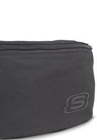 Bolsa de tela negra con una superficie texturizada y un cierre superior. Presenta un sutil logo en relieve en el costado. Diseño compacto y cilíndrico.