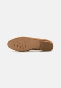 Mocasines de ante marrón con suela de goma plana, que presentan perforaciones para la transpirabilidad y un tacón texturizado para mayor agarre.