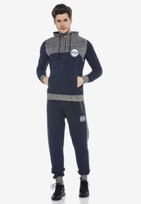 Marineblauer und grauer Kapuzenpullover mit Reißverschluss, strukturiertem Stoff und Vordertasche. Marineblaue Jogginghosen mit seitlichen Streifen und der Nummer "62".