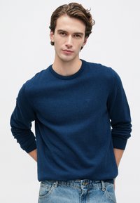 Μπλε πουλόβερ με στρογγυλή λαιμόκοψη από μαλακό ύφασμα, με ribbed μανσέτες και στρίφωμα. Συνδυασμένο με ανοιχτό μπλε τζιν. Διακριτική επωνυμία στο στήθος.