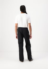 Black athletic pants with an elastic waistband and white side stripes, paired with a plain white T-shirt, viewed from behind.