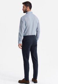 Camicetta blu a righe con colletto, abbinata a pantaloni blu navy. L'outfit presenta una vestibilità su misura e scarpe scure a contrasto.